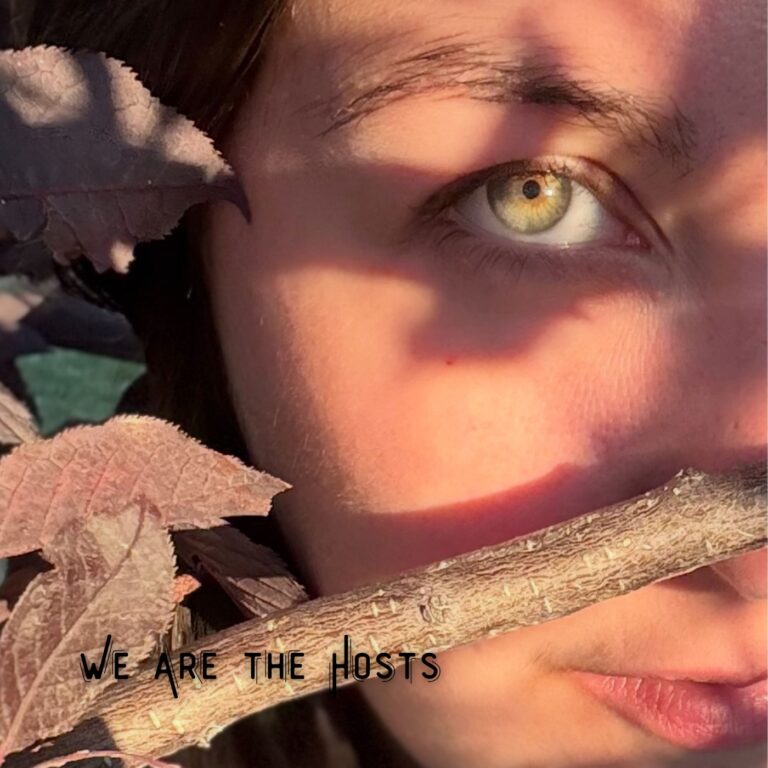 Image of half of Jacinda's face, with her eye in direct sunlight, and fall-colored leaves (browns and reds) to the left, with a branch crossing from lower left to mid right across the bottom half of her face. Text reads: "We Are the Hosts" in a sharper handwritten font, in the lower lefthand corner.
This is the album cover art for the single "We Are the Hosts" by Jacinda Wilson.